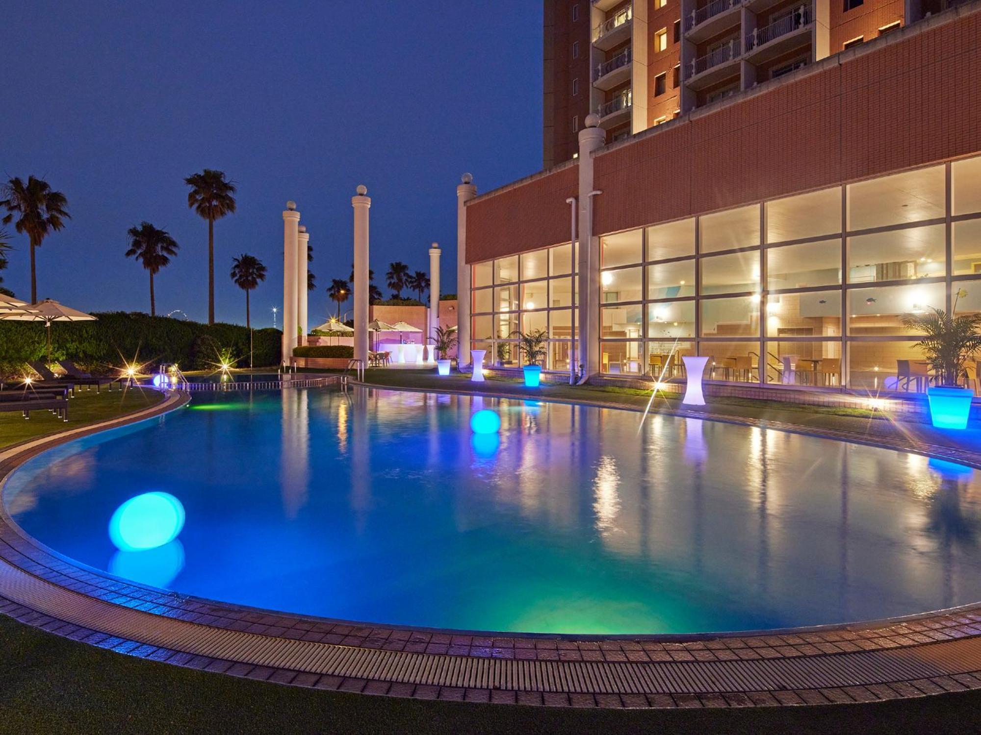 Grand Nikko Tokyo Bay Maihama Hotel Urayasu Екстериор снимка The photo shows a well-lit swimming pool at night, surrounded by a lush green area. The pool features glowing blue lights that create a serene and inviting atmosphere. Palm trees can be seen in the background, adding a tropical feel to the scene. Add